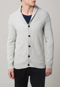 Svetle šedý pletený svetr s šálovým límcem, pěti černými knoflíky, žebrovanými manžetami a lemem. Textura je měkká a hladká s tkaným vzorem.