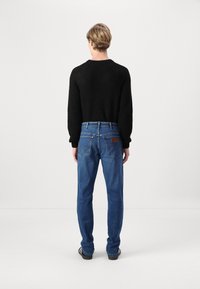 Czarny dzianinowy sweter, niebieskie dżinsy, pięć kieszeni, lekko zwężany krój oraz widoczne detale przeszycia na tylnych kieszeniach.