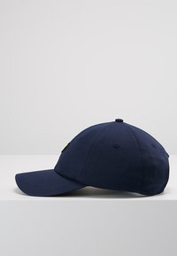 Granatowa czapka baseballowa z zakrzywionym daszkiem, wykonana z tkaniny z haftowanym emblematem z przodu oraz otworami wentylacyjnymi po bokach.
