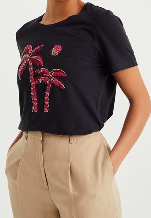 Sort t-shirt med korte ærmer med et palmetrædesign i rød og hvid broderi, kombineret med lys beige bukser med høj talje.