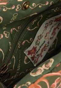 Zielona torba materiałowa z kwiatowym wzorem w różu i kremie. Posiada zamykaną na zamek kieszeń oraz metkę z napisem "Barbour" i "FARM RIO."