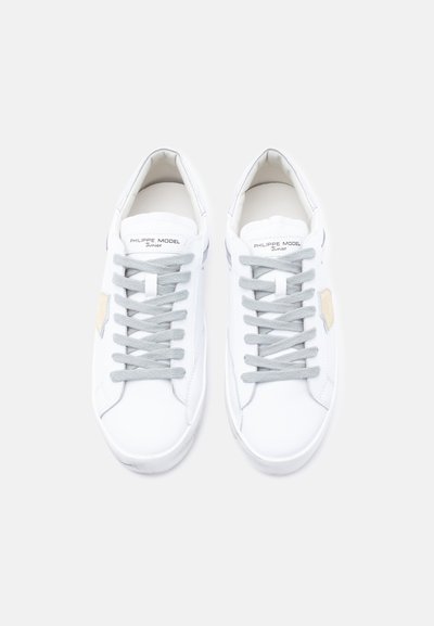 Λευκά αθλητικά παπούτσια από δέρμα με ομαλή υφή, με γκρι κορδόνια και διακριτική μπεζ λεπτομέρεια στο πλάι. Μινιμαλιστικός σχεδιασμός σε όλο το μήκος.