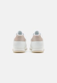 Baskets blanches avec une tige en cuir lisse, présentant un accent beige clair au talon, un col rembourré et une semelle en caoutchouc texturée.