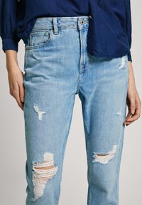 Šviesiai mėlynos džinsinės kelnės su nunešimais, įskaitant kelis įplyšimus ir nusitrintus kraštus. Laisvas siluetas ir vidutinio aukščio juosmens dizainas.