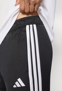 Μαύρο αθλητικό παντελόνι από διαπνέον υλικό, με τρεις κάθετες λευκές ρίγες και μικρό λευκό λογότυπο στο κάτω αριστερό μέρος.