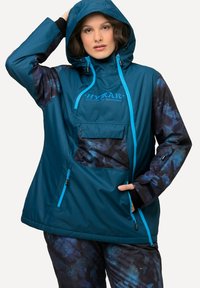 Windbreaker in teal con dettagli blu, dotato di cappuccio, tasca frontale e maniche a motivo astratto scuro. Realizzato in materiale leggero e resistente all'acqua.