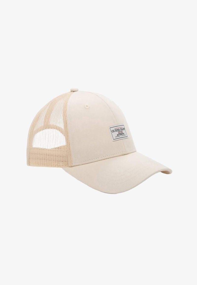 Casquette de baseball beige avec panneaux arrière en maille et une étiquette frontale portant l'inscription "Guess Jeans Authentic."