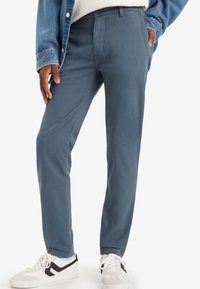 Blå byxor i bomullsblandning med slim fit, med sidofickor och en ren design, i kombination med vita sneakers och en jeansjacka.