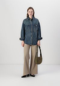 Jeanskjorte med to brystlommer, lyseblå farge, knapper i front. Beige utsvingte bukser, svarte lakk-sko og en grønn skulderveske.