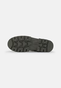 Soletta di scarpa con un battistrada a motivo. Realizzata in gomma, presenta scanalature profonde e bordi arrotondati. Colore: grigio scuro. Marchio visibile sulla suola.