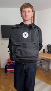 Černý plátěný batoh s dvojitými horními úchyty, nastavitelnými popruhy, přední kapsou na zip a kulatou odznakem s logem Converse. Texturovaná tkanina.