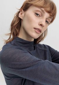 Dunkelgraues Longsleeve-Oberteil mit hohem Kragen. Der Stoff wirkt weich und hat einen leichten Glanz. Das Design verfügt über eng anliegende Ärmel und minimalistische Linien.