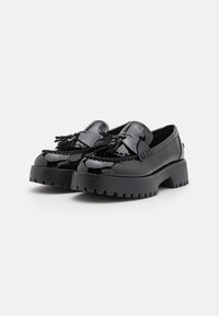Mocassins en cuir verni noir avec une semelle épaisse et des glands décoratifs à l'avant. Présente un design de couture détaillé.