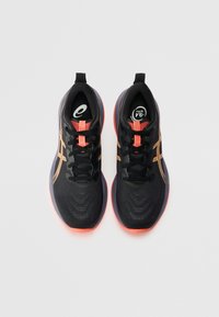 Black athletic shoes with orange accents, mesh upper, textured surface, and a contrasting vibrant sole, featuring black laces and logo.