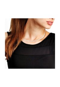 Collier de perles blanches à la texture lisse, porté sur un haut noir, se posant juste au-dessus de la clavicule, composé de perles sphériques uniformes.