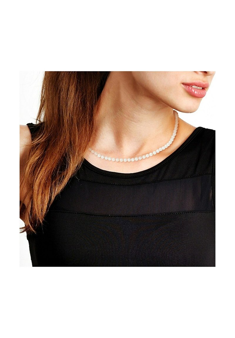 Collier de perles blanches à la texture lisse, porté sur un haut noir, se posant juste au-dessus de la clavicule, composé de perles sphériques uniformes.