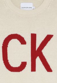 Krémový pletený svetr s velkým červeným logem "CK". Hladká textura s žebrovaným výstřihem a lemem. Značka: CALVIN KLEIN JEANS. Velikost 8.