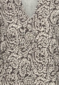 Gros plan sur un vêtement à col en V avec un tissu épais à motifs floraux et feuillages noir et blanc. Aucun bouton, fermeture éclair ou accessoire visible.
