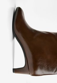 Bottines en cuir marron avec un bout pointu, une silhouette incurvée et un accent de talon noir. Texture lisse et design moderne et épuré.