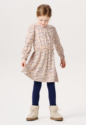 Robe florale rose avec des manches longues, taille froncée et col volanté. Associée à des leggings côtelés marine et des bottes en fausse fourrure beige.