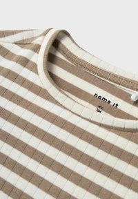 Koszulka w paski z okrągłym dekoltem, z naprzemiennymi beżowymi i białymi poziomymi paskami. Tekstura prążkowana; metka mówi "name it" i rozmiar 104.