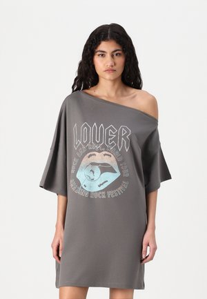 Grå oversized klänning med off-shoulder design. Har ett stiliserat grafiskt tryck av läppar och text i kontrasterande färger. Mjuk tyg.