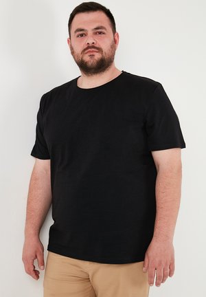 Fekete, rövid ujjú pamut póló; kerek nyakú; sima textúrájú; világos barnás nadrággal viselve.