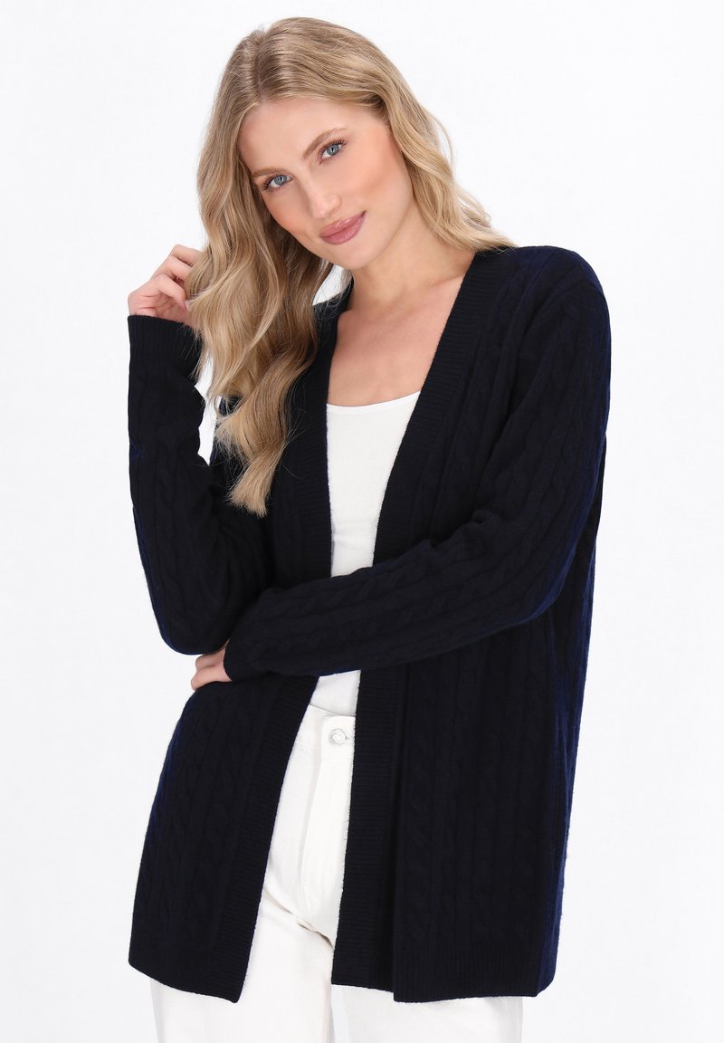 Marinblå kabelstickad cardigan med öppen front, långa ärmar, ribbad mudd och nederkant. Mjuk textur, avslappnad passform, passar bra med ljusa toppar.