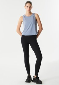 Lichtblauw mouwloos sporttop met een ronde hals, gecombineerd met zwarte leggings. De leggings zijn aansluitend en hebben een gladde textuur.