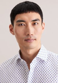 Wit shirt met blauwe stippen, knoopsluitingskraag en korte mouwen. De stof lijkt glad met een lichte, ademende textuur.