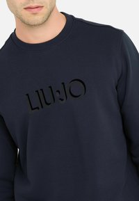Marineblaue Sweatshirt aus Baumwolle mit Rundhals; verfügt über ein tonal gesticktes Logo 'LIU:JO' auf der Vorderseite. Glatte Textur.