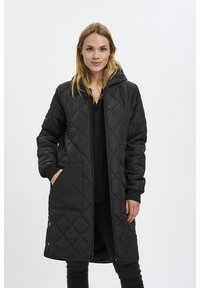 Manteau long matelassé noir avec capuche, doté de deux poches avant, de poignets côtelés et d'une fermeture éclair à l'avant. Tissu lisse et texturé.