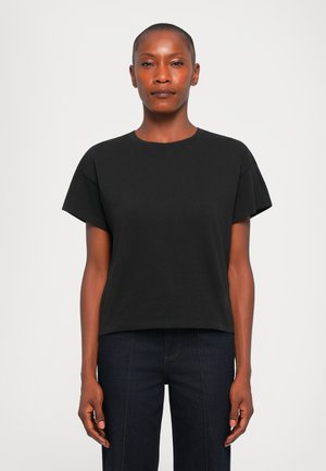 Black cotton t-shirt with short sleeves, round neckline, relaxed fit, and smooth texture. Paired with dark denim pants.