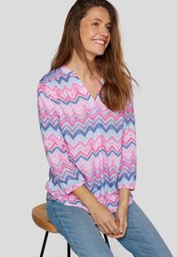 Multifarbene Bluse mit pinken und blauen Zickzackmustern, V-Ausschnitt und dreiviertellangen Ärmeln, aus leichtem Stoff gefertigt.