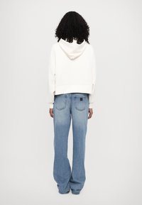 Felpa bianca cropped con cappuccio regolabile abbinata a jeans a gamba larga di colore azzurro chiaro, dotati di tasche posteriori e una finitura testurizzata.