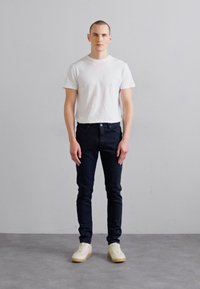 Bela kratka majica s kratkimi rokavi, temni ozki jeans in smetana teniske. Obleka ima preprost dizajn s čistimi, modernimi silhuetami.