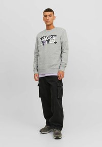 Sudadera gris con un estampado gráfico en púrpura y negro, combinada con pantalones cargo negros holgados y zapatillas grises.