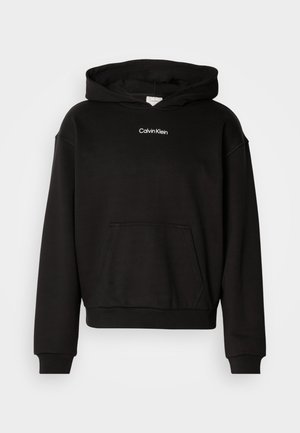 Čierna mikina s kapucňou a predným kloktacím vreckom, rebrované manžety a biele vyšívané logo "Calvin Klein" na hrudi.
