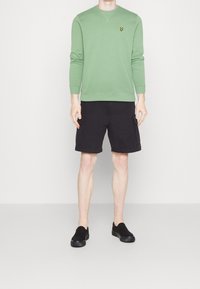 Groene katoenen sweatshirt met een ronde hals en lange mouwen; zwarte cargoshorts; zwarte instap-schoenen. Bevat een logo op de borst.