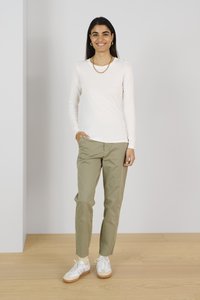 Weißes langärmliges Oberteil, olivgrüne Hose und weiße Sneakers mit hellen Sohlen. Einfaches Design, taillierte Silhouette und leichte Textur.