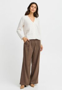 Ljusbeige cardigan med V-hals, strukturerat prickmönster och fem knappar; ihop med bruna vida byxor och beige klackar.