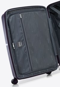 Interno della valigia rigida viola con fodera in nylon grigio, tasca in rete con zip e modelli di viaggio stampati. Presenta ruote doppie per una maggiore mobilità.
