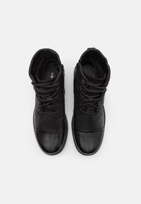 Bottes de cheville en cuir noir avec lacets robustes, accents en métal, texture lisse et intérieur rembourré pour le confort.