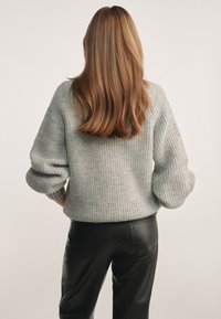 Szary, dziergany sweter o luźnym kroju i szerokich rękawach, w zestawieniu z wąskimi, czarnymi skórzanymi spodniami. Gładka faktura i minimalistyczny design.