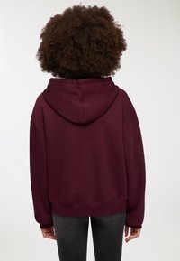 Felpa con cappuccio bordeaux a vestibilità rilassata, con polsini e orlo a costine, realizzata in tessuto morbido, dotata di un ampio cappuccio e di una tasca a marsupio.