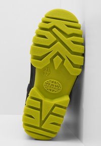 Semelle de chaussure noire avec un motif de bande de roulement jaune prononcé. Comprend le logo "RAW TERRAIN" et une empreinte de taille au bas. Texturée pour une meilleure adhérence.