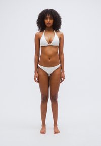Σετ λευκό μπικίνι με τριγωνικό τοπ και χωρίς ραφές κάτω μέρος. Λείο ύφασμα, μινιμαλιστικός σχεδιασμός, χωρίς ορατά μοτίβα ή μεταλλικά στοιχεία.