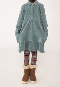 Abito di velluto a coste di colore verde acqua, con colletto, maniche lunghe e orlo arricciato. Abbinato a leggings a righe multicolori e stivali marroni foderati di pelliccia.