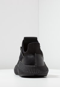 Black athletic shoe featuring a textured knit upper, a sturdy heel tab, a smooth leather overlay, and a ridged rubber sole.