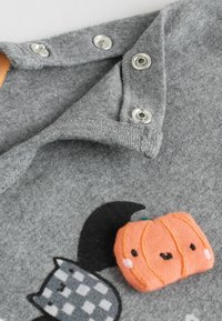 Grå stof med trykknapper, med et smilende orange græskarmønster og dele af et sort-hvidt katte design.